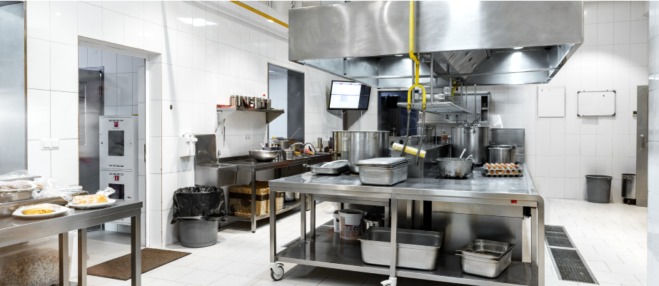 A spacious commercial kitchen with stainless steel workstations, large cooking pots, ventilation hoods, and neatly arranged equipment.